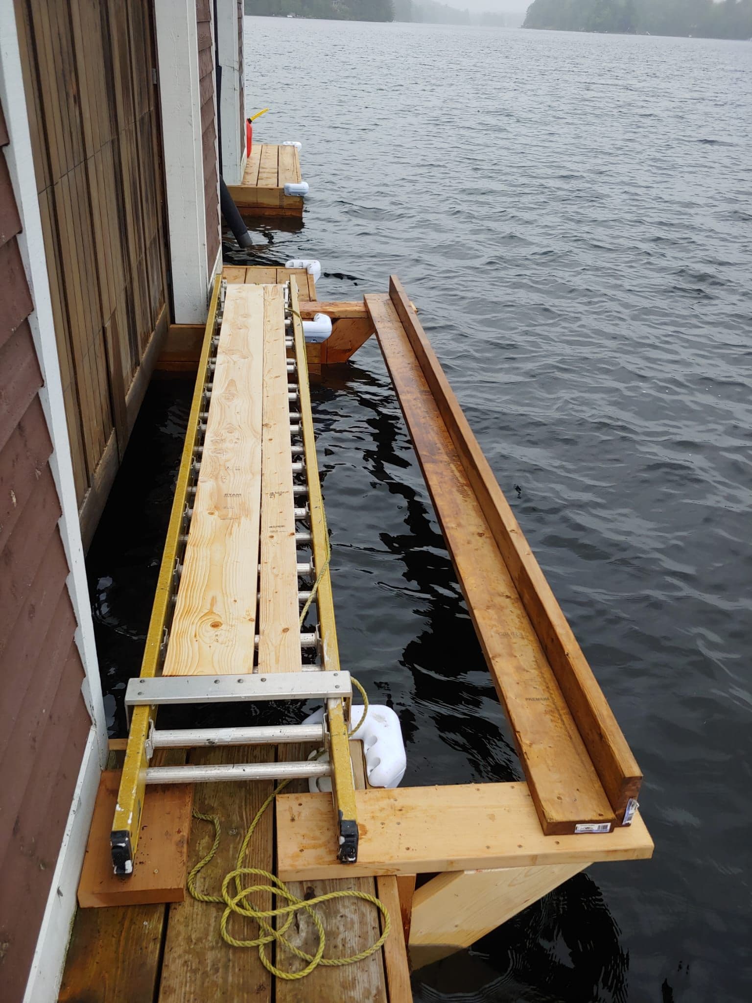 Planked staging set along a dock beside a cedar boathouse on a Muskoka lake, floats under the platform, before painting