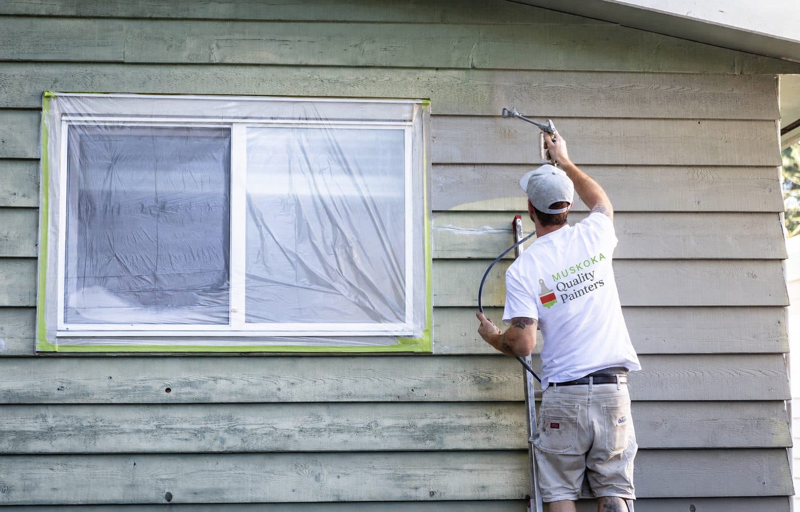 A Muskoka Quality Painters crew member spraying a prepped exterior wall, windows masked off
